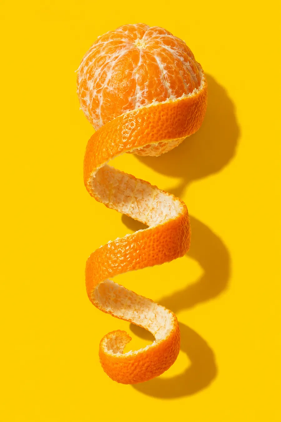 An orange with its peel cut into one long spiral strip, on yellow